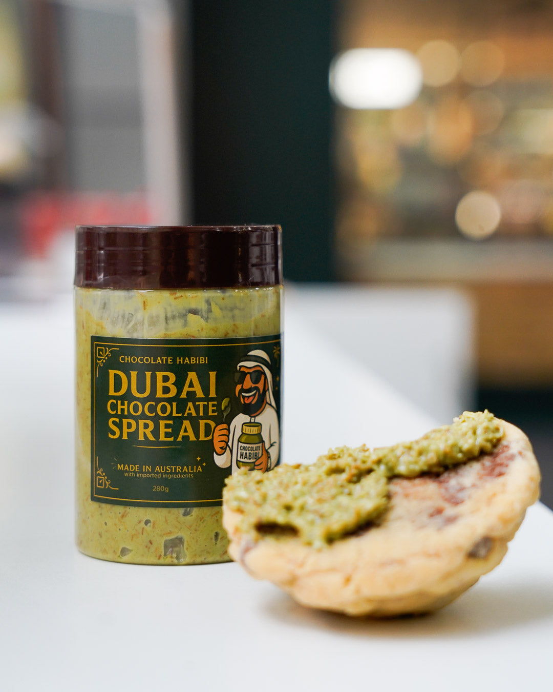 Jar of Dubai Chocolate Spread with a pistachio cookie on a white surface in a café setting