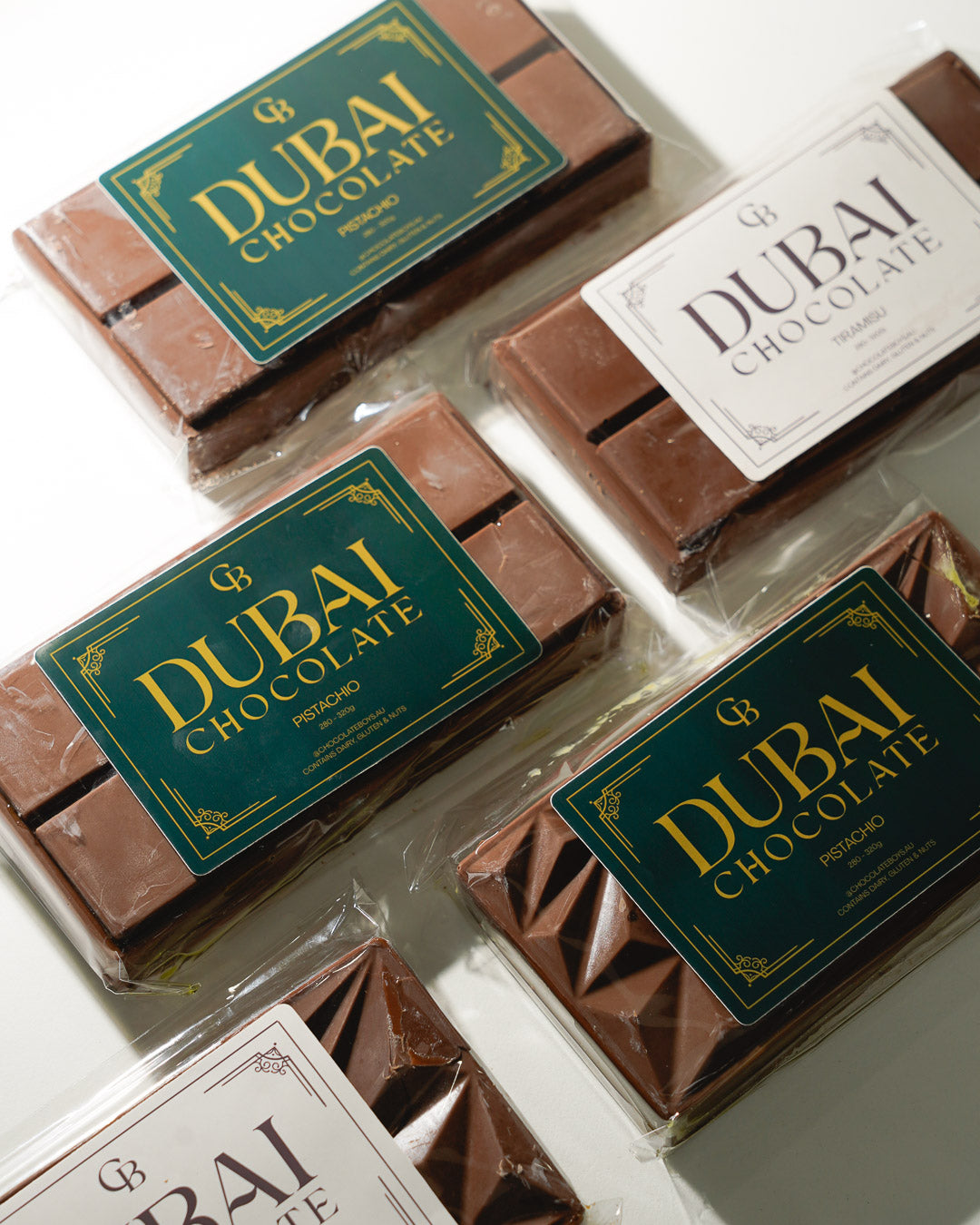 Flat lay of multiple Dubai Chocolate bars featuring pistachio and tiramisu flavours with elegant green and white packaging on a light background