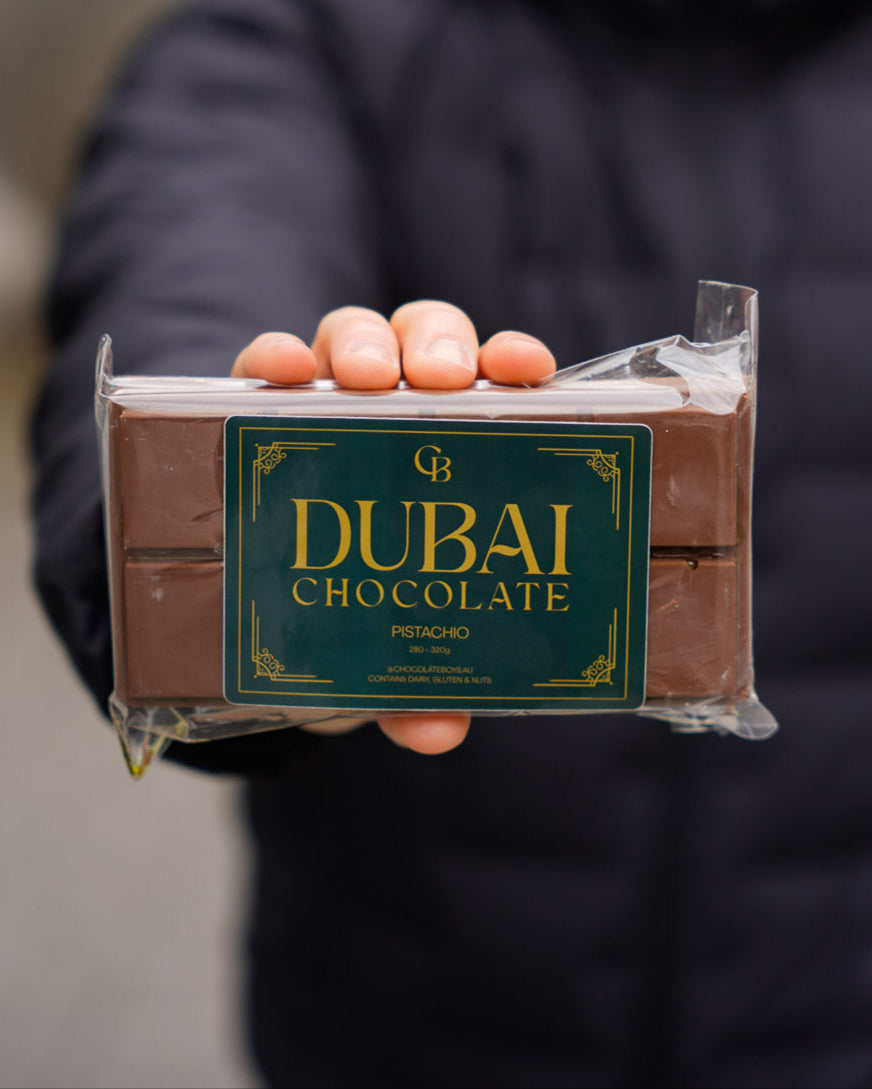 Person holding a Dubai Pistachio Chocolate bar with emerald green packaging, focused on product branding with blurred background