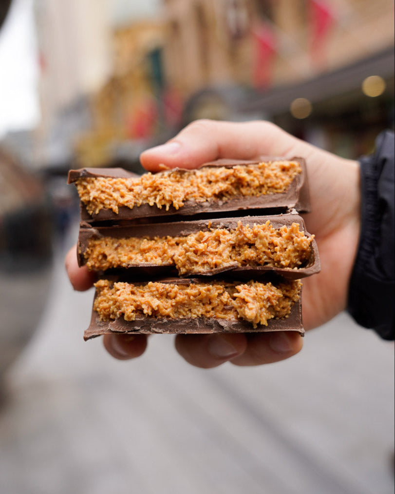 Hand holding stacked tiramisu-filled Dubai chocolate bars with creamy, textured center and glossy chocolate shell, street background