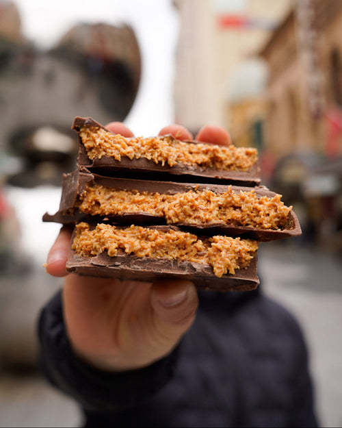 Hand holding stacked tiramisu-filled Dubai chocolate bars with creamy, textured center and glossy chocolate shell, street background